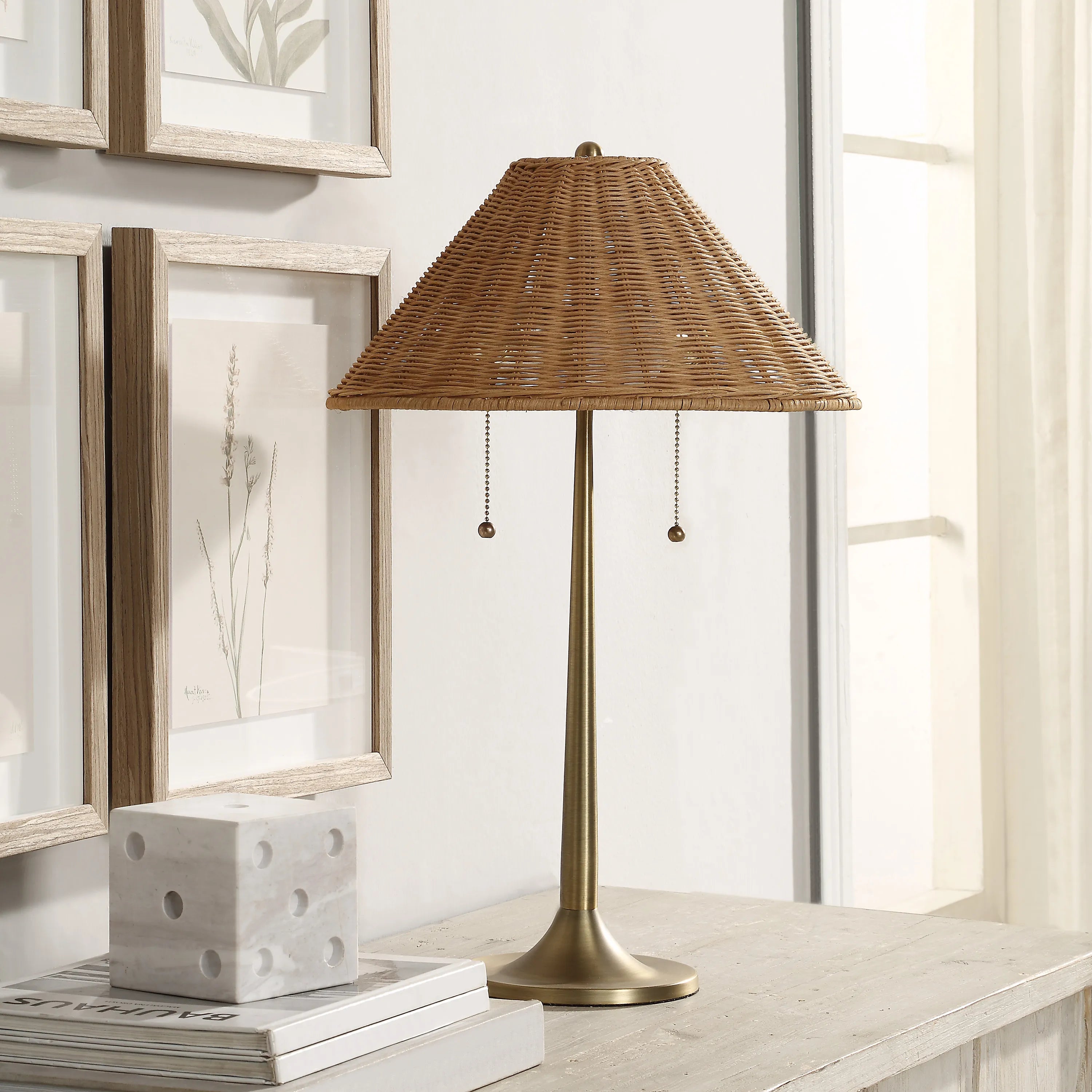 Solara Rattan Glow Table Lamp with woven rattan shade on wooden table beside framed wall art and decor books