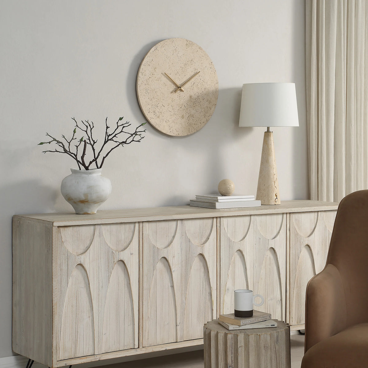 Solea Travertine Wall Clock displayed above rustic sideboard with ceramic vase and table lamp