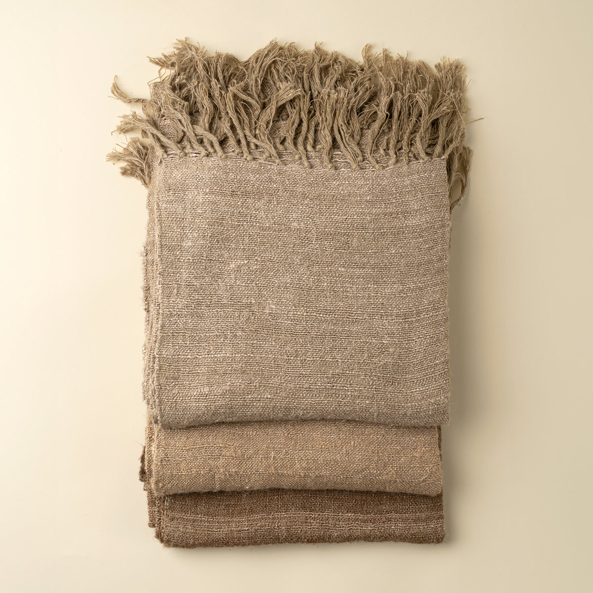 Folded beige blanket with frayed edges on a beige background