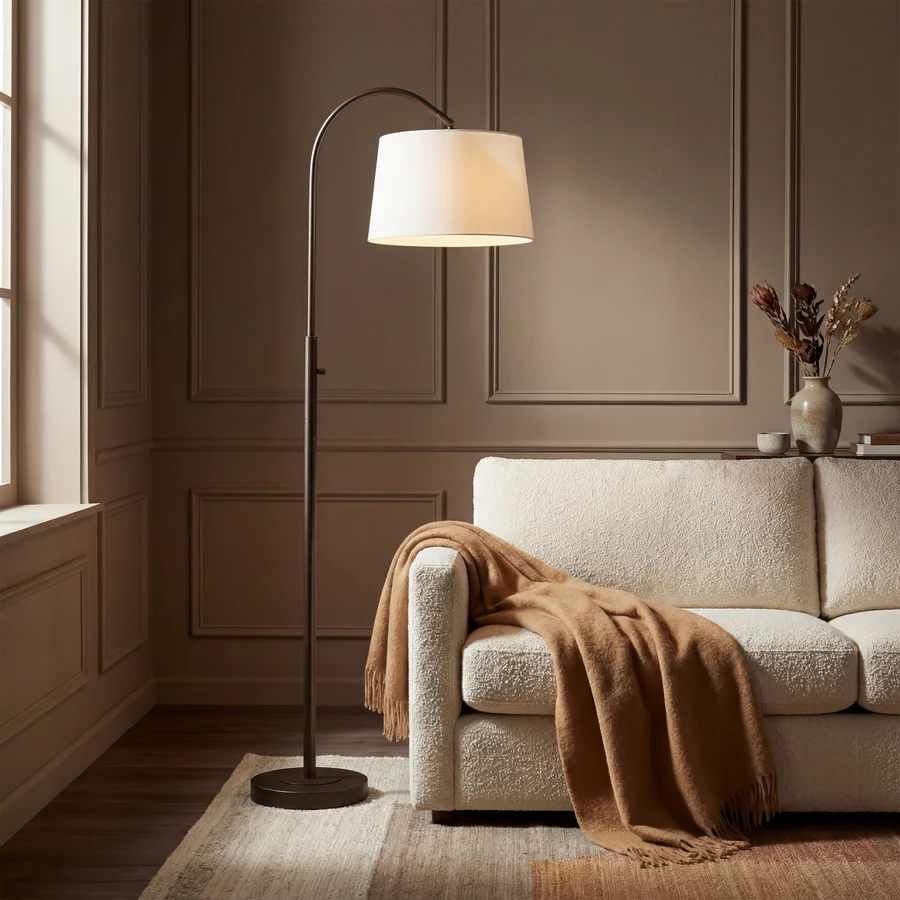 Solenne Arc Floor Lamp in painted bronze styled beside a cream sofa in a warm living room.