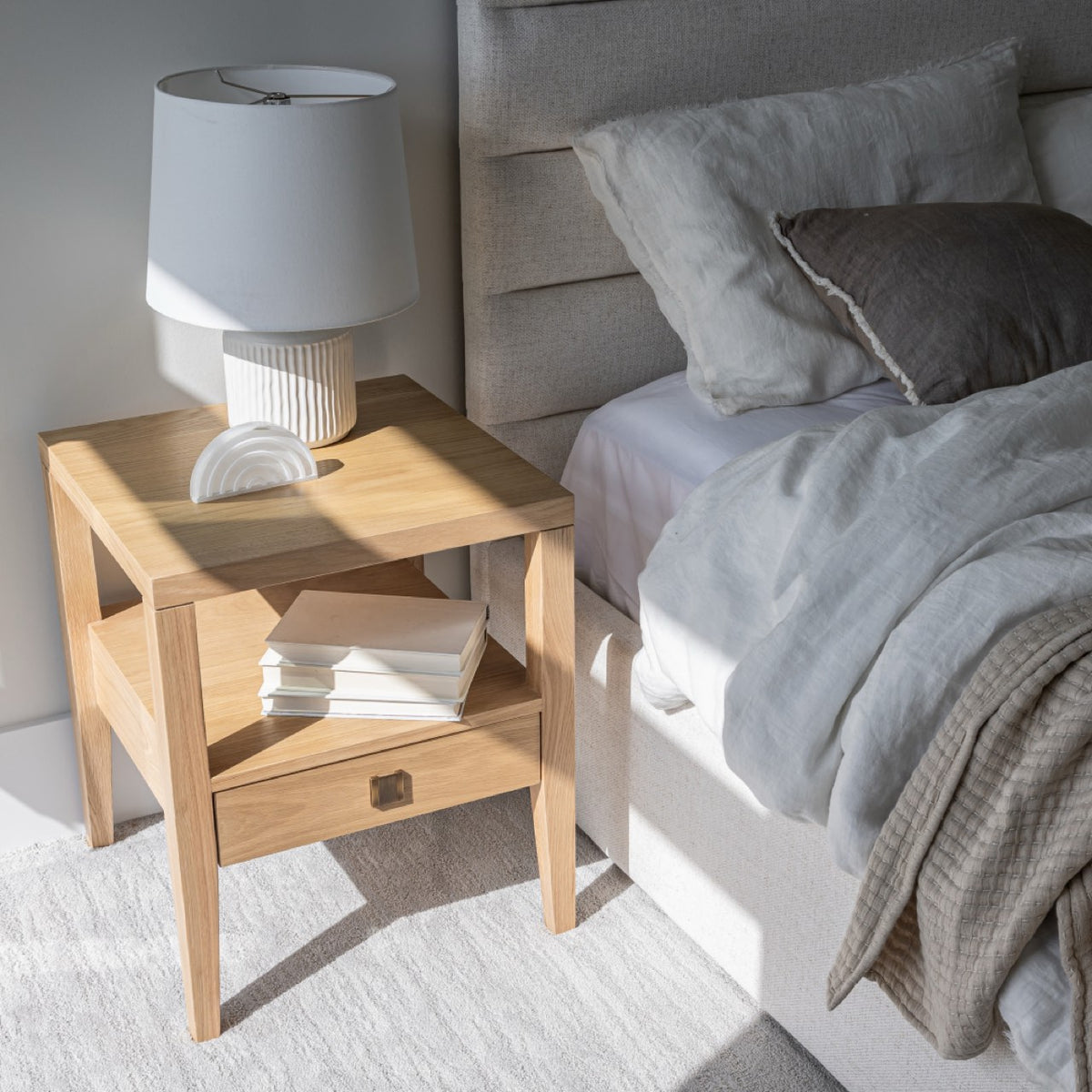 High-angle lifestyle shot of the Sutton oak nightstand styled with neutral bedding and natural decor.