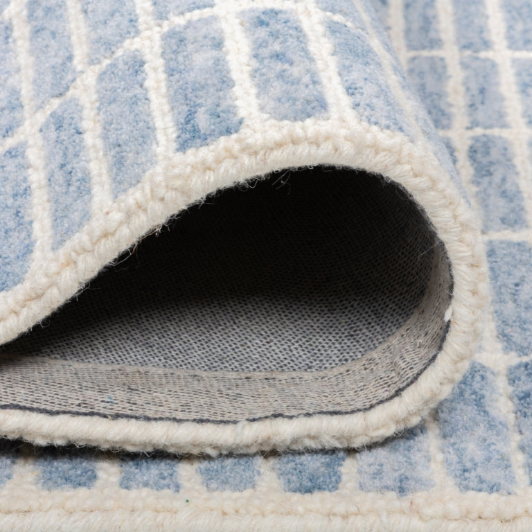Folded Tessera Hand-Tufted Wool Grid Rug in blue showing the wool pile, bound edge, and cotton backing.
