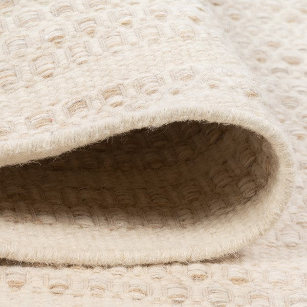Folded edge view of the ivory Theo wool rug, demonstrating the thick woven pile and reversible hand-woven construction without canvas backing
