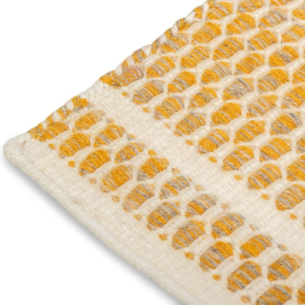 Close-up of the woven edge and border detailing on the mustard yellow and cream Theo hand-woven wool rug.