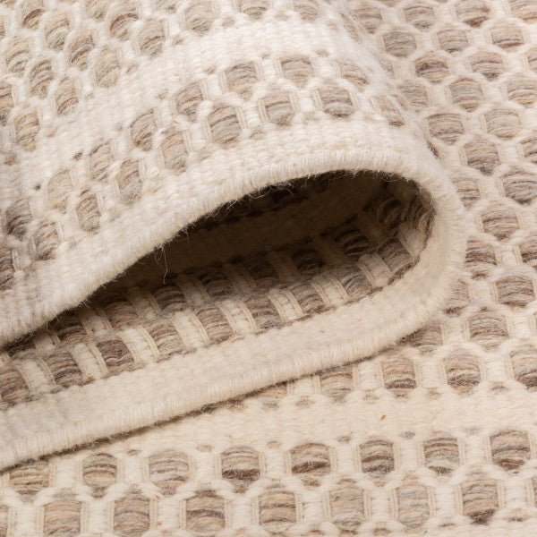 Folded edge view of the husk Theo wool rug, showing the plush thickness of the chunky woven design and the raw hand-woven underside.