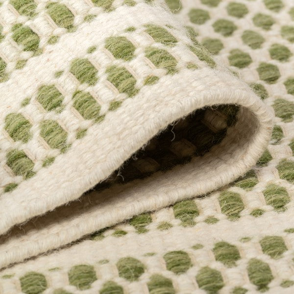 Soft draped folds of the sage green Theo wool rug showcasing its flexible woven geometric pattern.