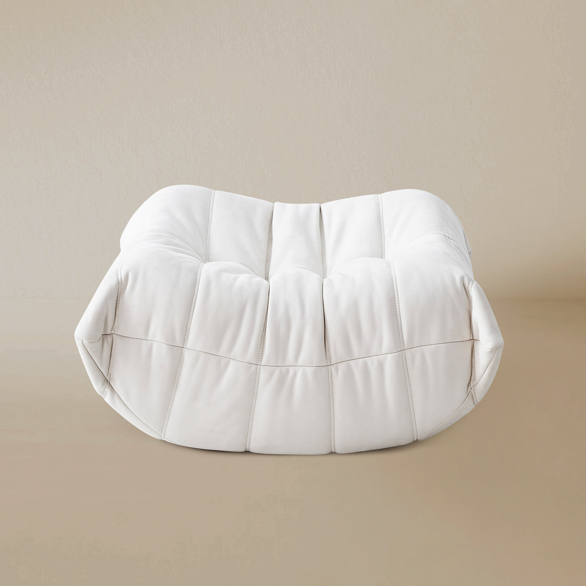 Side view of the White TOGO ottoman on a beige background