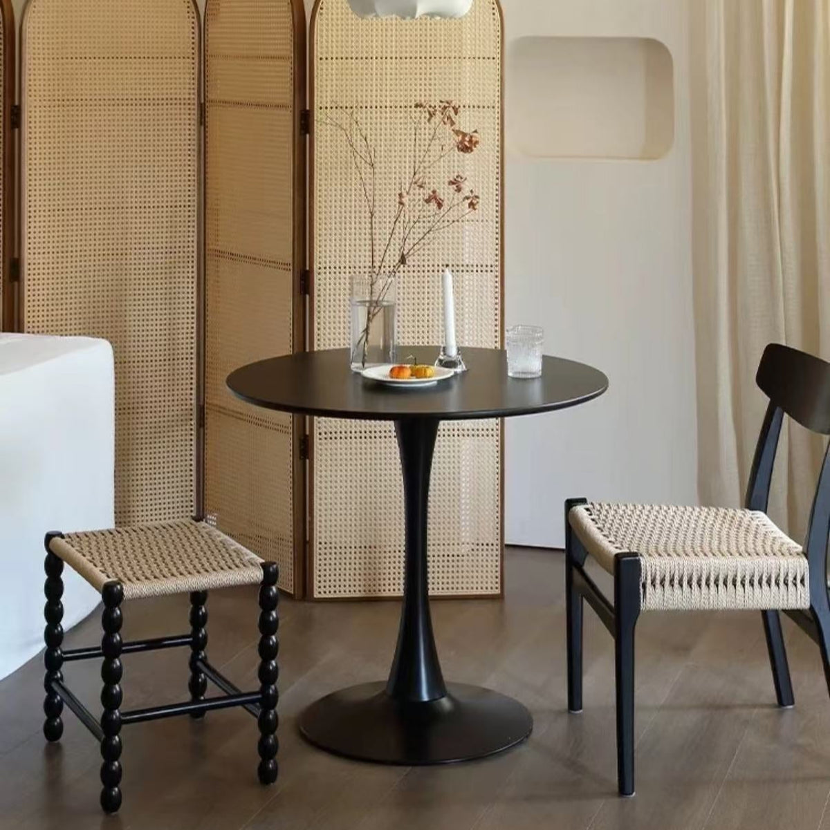 Black Tulip Dining Table in a modern home setting with woven chairs, rattan screen, and minimalist tabletop decor