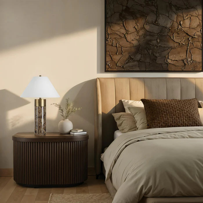 Neatly made bed with pillows, nightstand with lamp, and abstract wall art in a bedroom setting.