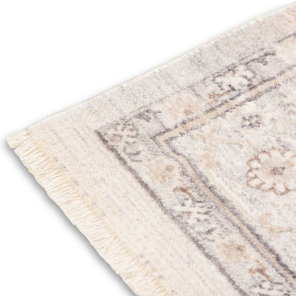 Corner view of the neutral Verona area rug highlighting its distressed floral border pattern, bound side edge, and short fringe detailing.