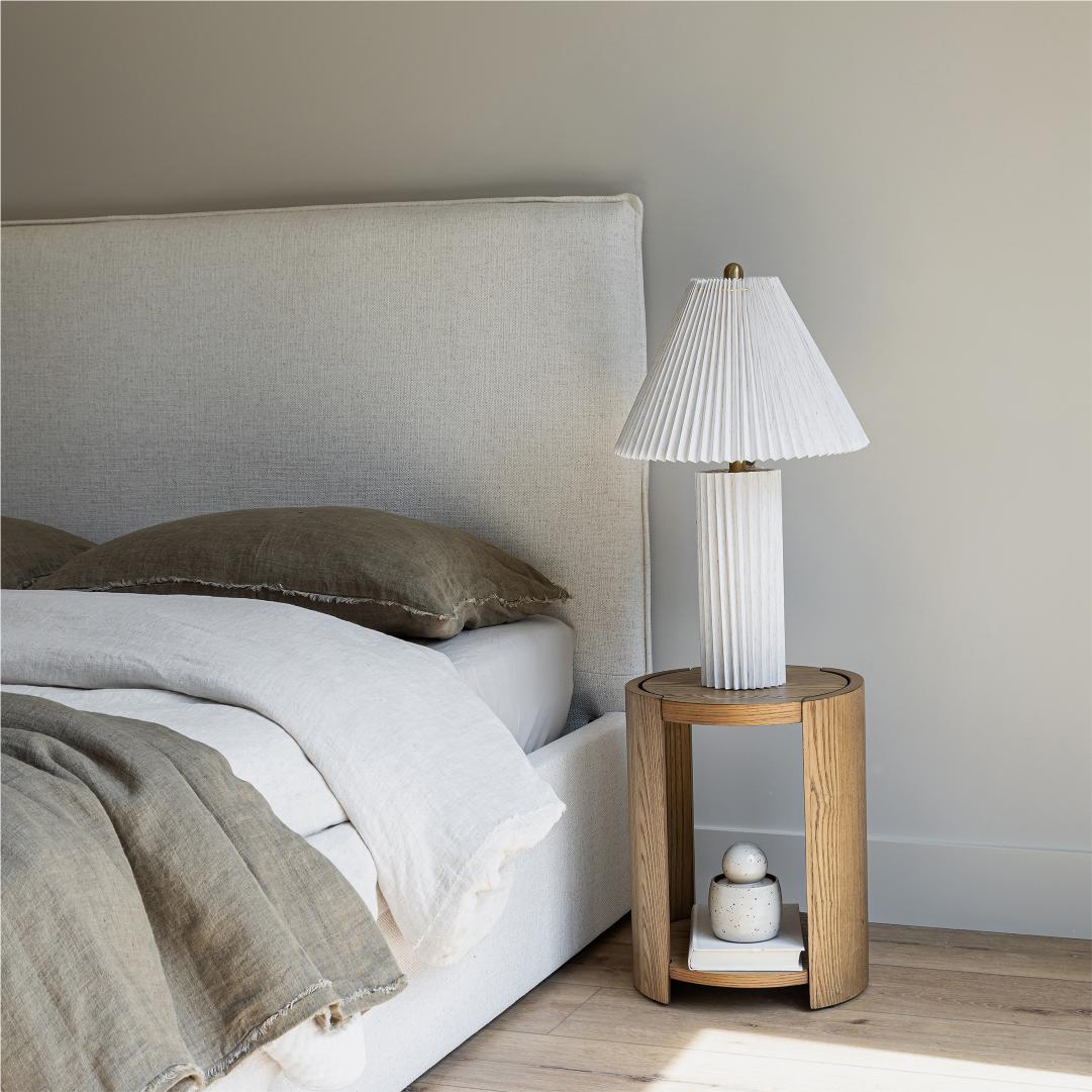 The Vivienne French-seamed bed styled in a neutral bedroom with olive green linen bedding and a fluted side table