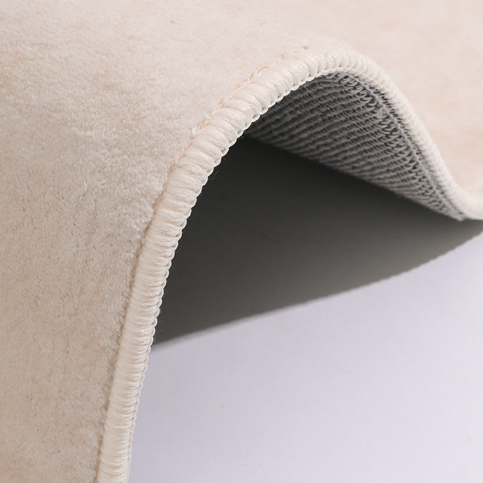 Close-up of the Woven Whisper Rug showing its soft beige surface, rounded edge, and flexible backing detail.