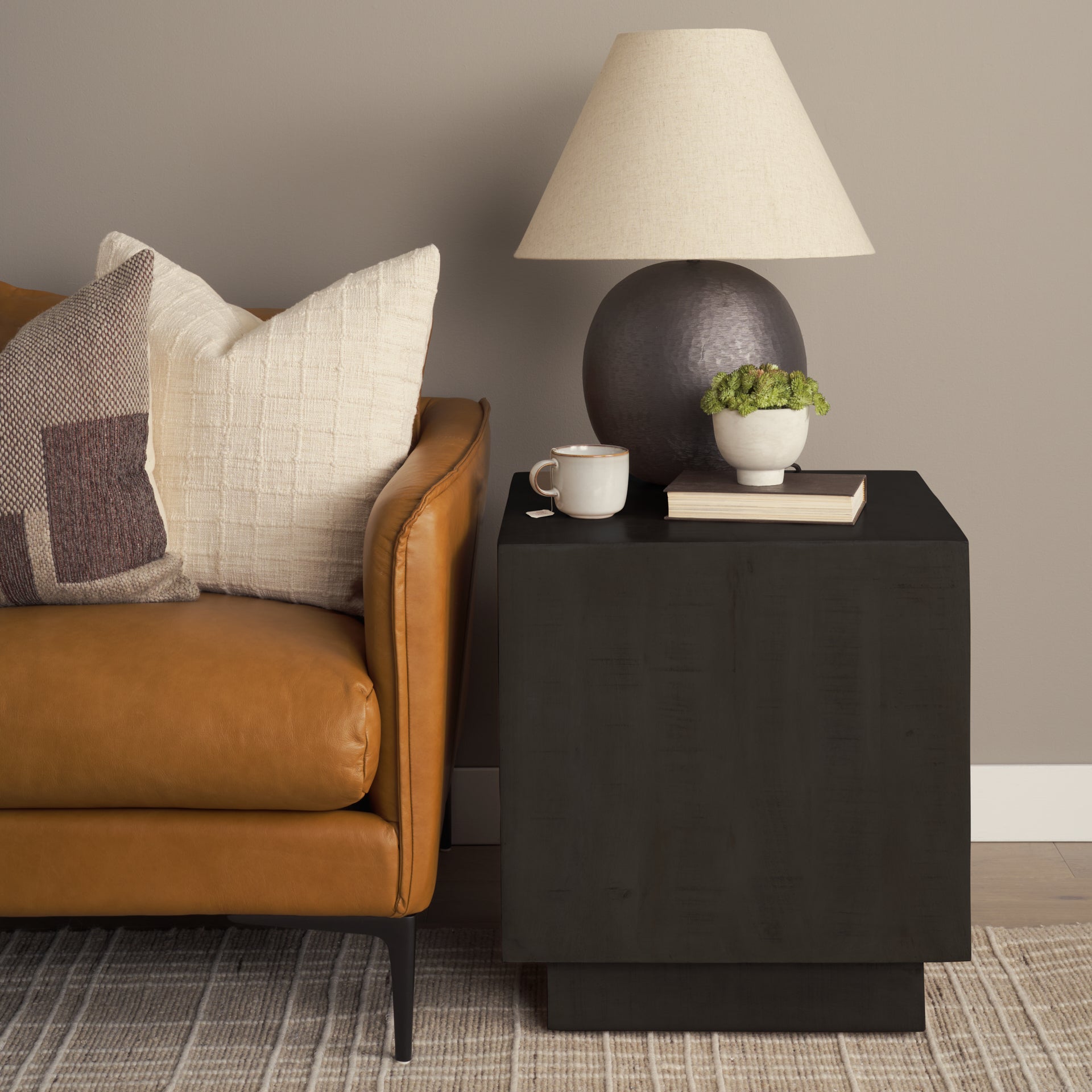 Dark brown side table with lamp, mug, and plant next to a brown leather sofa.