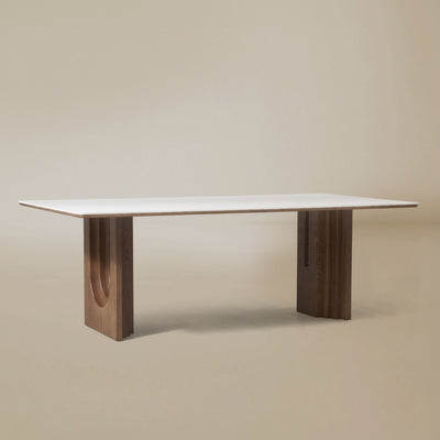 Angle view of the Arcadian Dining Table with a white travertine top and walnut wooden legs on a beige background