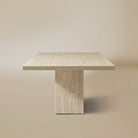 Side view of the natural travertine Ardella dining table on a beige background