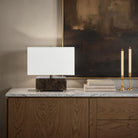 Modern lamp on a marble surface with candles and books against an abstract painting.