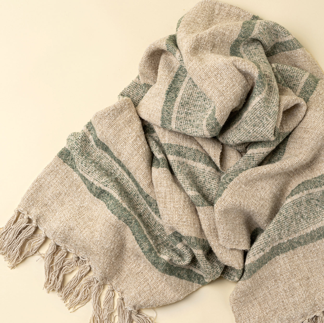 Textured scarf with green stripes and tassels on a beige background