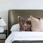 A styled bedroom scene showing the Aveline Velvet Bed with a tall upholstered headboard, white bedding, and two decorative pillows in front