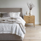 Wide view of the Beaumont 3-Drawer Nightstand in a modern bedroom with light oak flooring. The nightstand is styled with tall decorative branches in a textured vase.