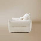 Bella Boucle Sofa in cream boucle fabric, shown from a rear angle with matching throw pillows, set against a warm beige studio background.