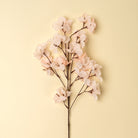Artificial flower branch with pink flowers on a light yellow background