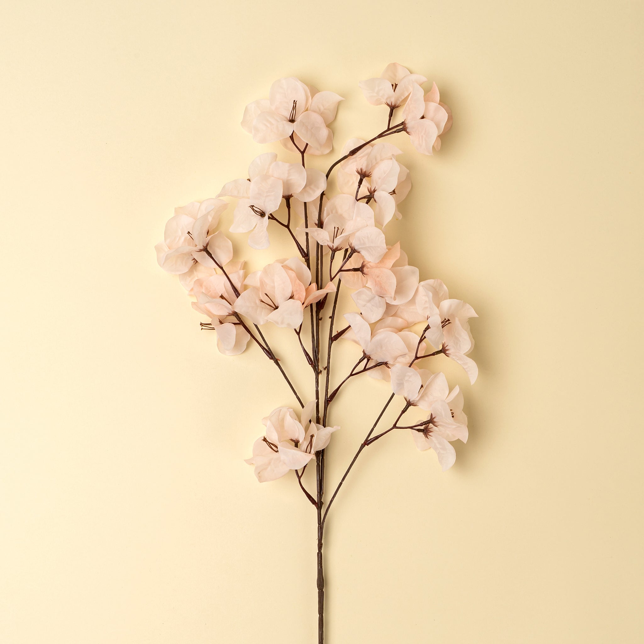 Artificial flower branch with pink flowers on a light yellow background