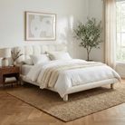 Neatly made bed in a bedroom with a plant and framed art on the wall.
