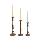 Caldria set of three antique brass-finished candle holders shown with ivory taper candles against a white background.