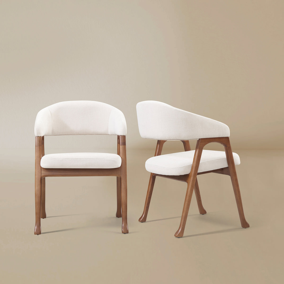 Two Calira linen dining chairs with wraparound upholstered backs, ash wood veneer frames and flared feet on a warm beige background