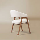Angled rear view of the Calira linen dining chair showing its curved upholstered backrest and splayed wood legs
