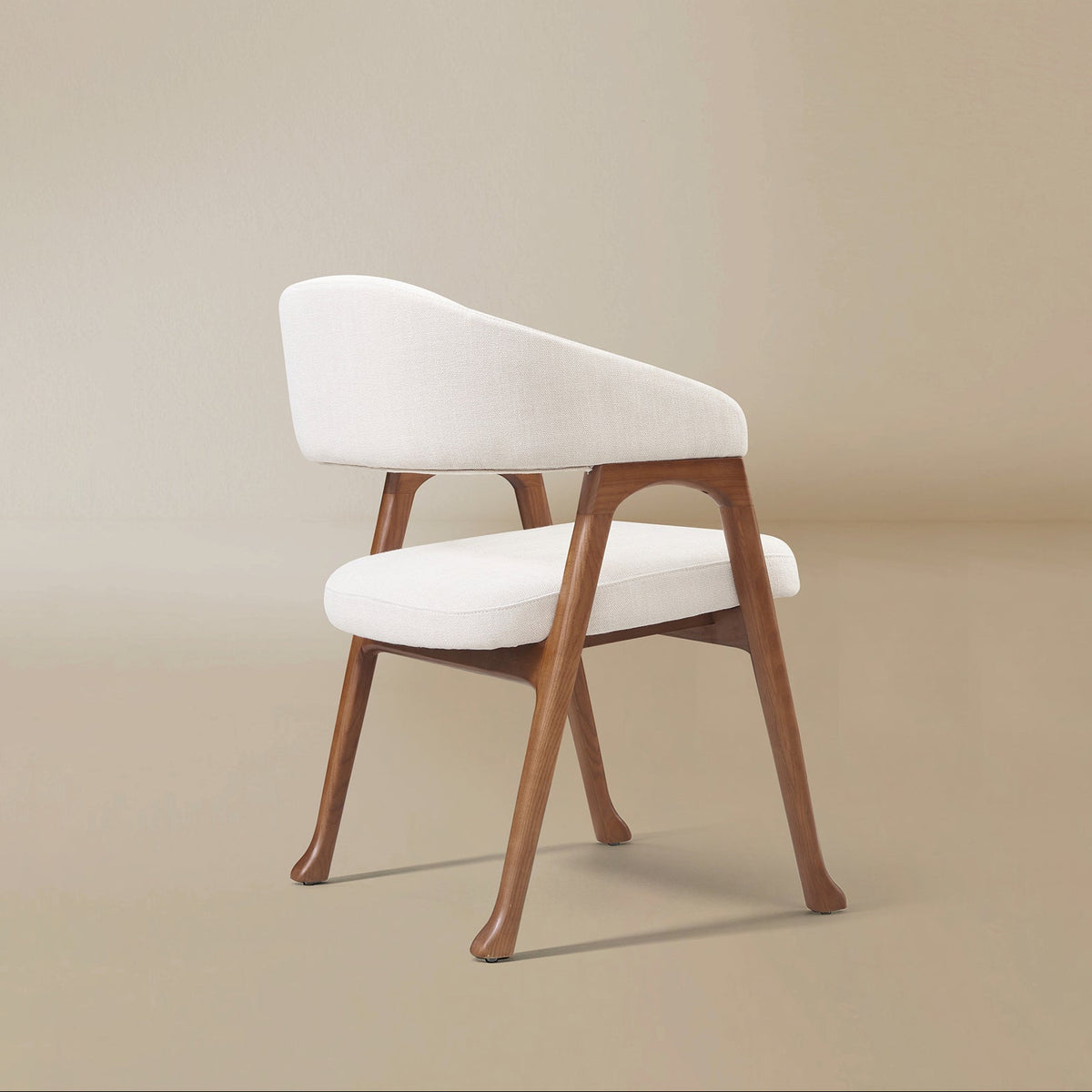 Angled rear view of the Calira linen dining chair showing its curved upholstered backrest and splayed wood legs