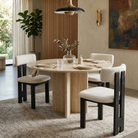 Three white bouclé and black ash wood dining chairs styled around a modern round light stone dining table in an elegant dining room featuring the Casper...