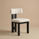 Angled view of the bouclé dining chair showing its curved backrest, plush white textured upholstery, and matte black ash wood legs featuring the Casper...