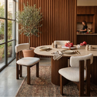 White bouclé dining chairs with dark wood frames styled at a round table in a contemporary open-concept space featuring a fluted wood accent wall featuring...