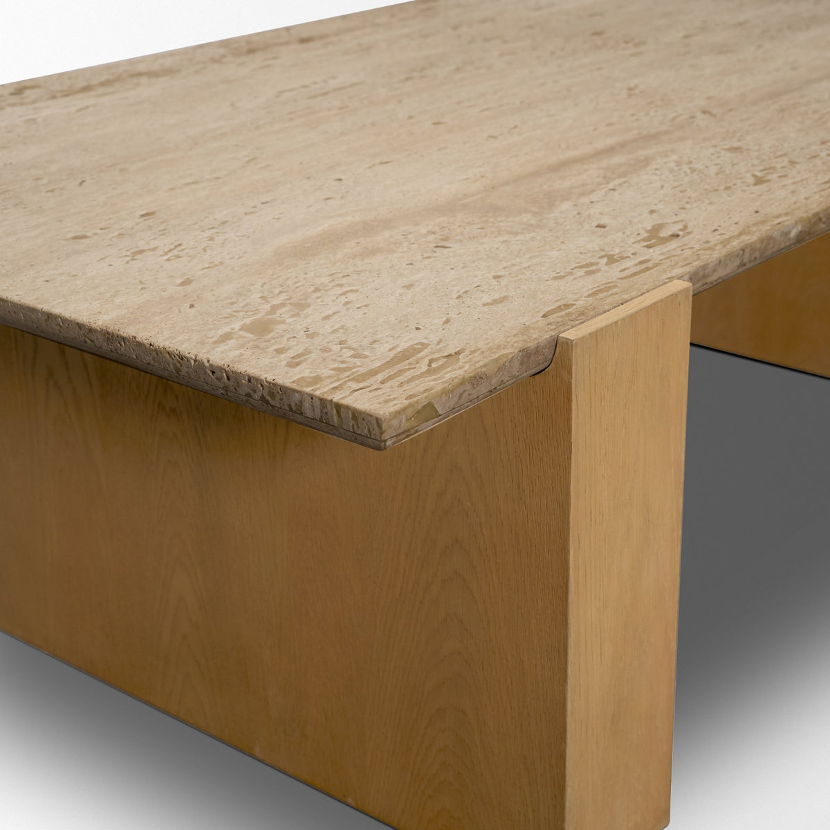 Close-up corner detail of the Cavelle Coffee Table showing the travertine top profile where it meets the solid oak blade leg.