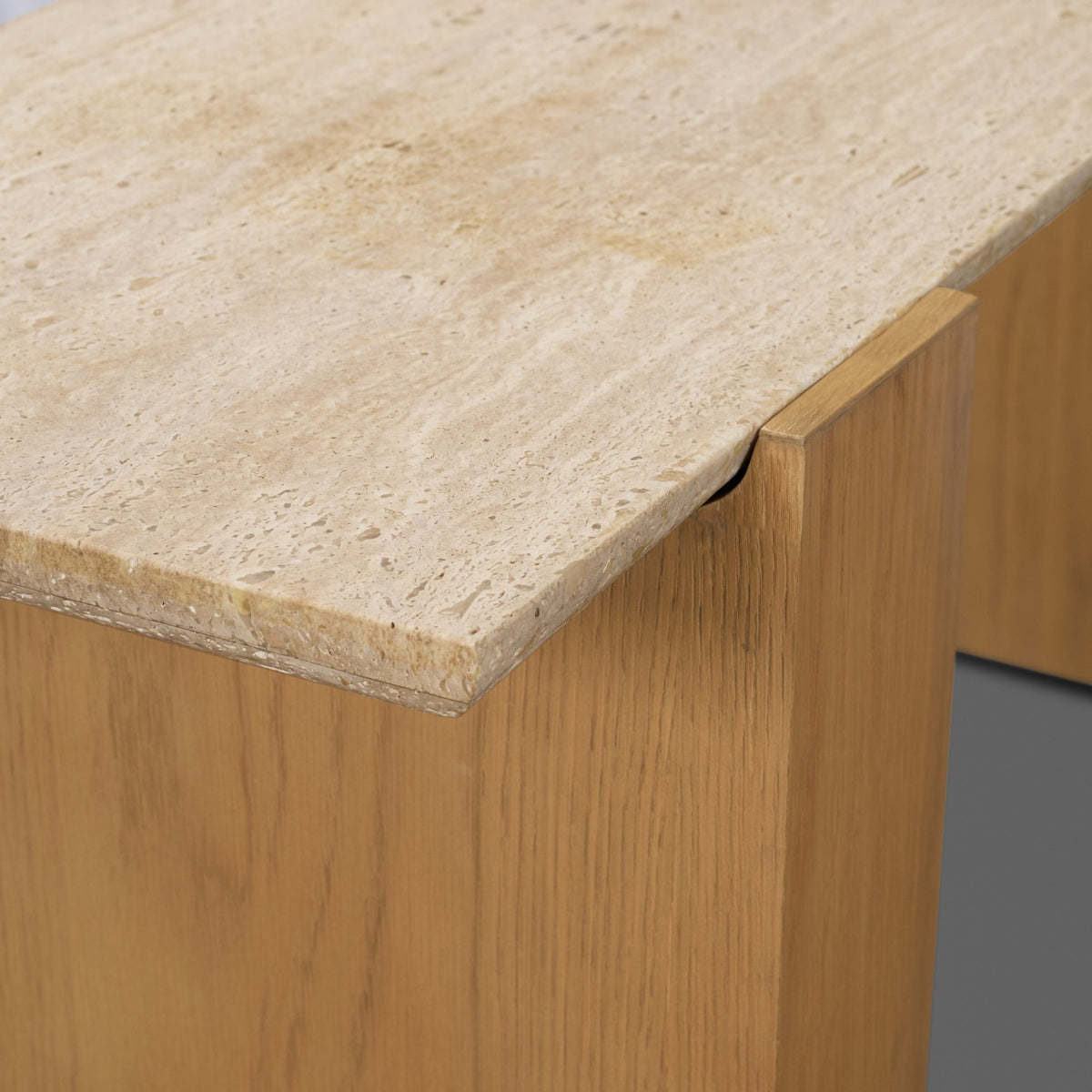 Close-up corner detail of the Cavelle Console Table showing the travertine edge profile where it meets the solid oak blade leg.