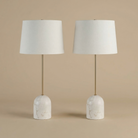 A pair of Celine table lamps featuring dome-shaped white marble bases, slender brass stems, and white linen shades.
