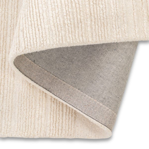 Close-up of the folded Claire Hand-tufted rug showing a textured cream-colored top surface and a heather gray underside with a stitched edge.