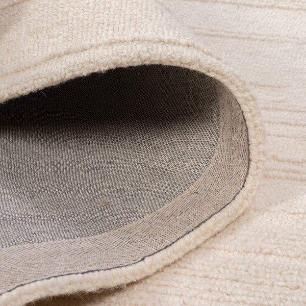 Close-up of the Claire Hand-tufted rug with a rolled corner showing the underside and inner border.