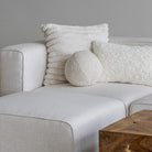 The Cloudline textured cushion trio styled on a cream bouclé sectional sofa next to a live-edge wood coffee table.
