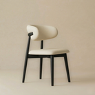 Angled view of the black Modern Leather Ash Wood Dining Chair highlighting the unique wrap-around backrest and tapered black wooden legs.