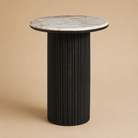 Round side table with marble top and ribbed black base on a beige background