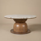 Front view of the Ottille round coffee table with marble top and wooden base on a beige studio background