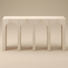Elio Travertine Console Table in a matte beige finish, featuring repeating architectural archway cutouts shown from an angled perspective.