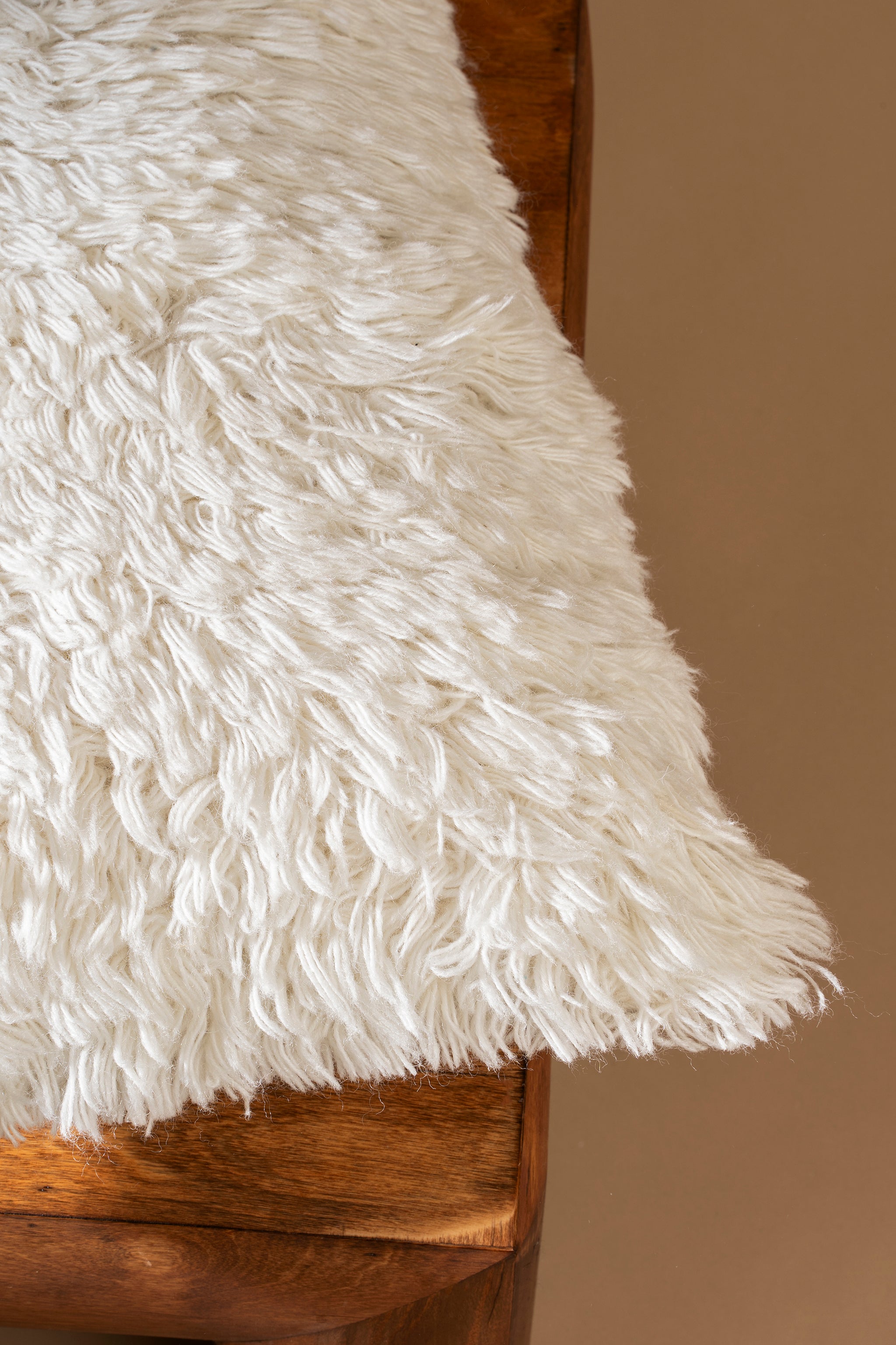 Close-up of a fluffy white rug on a wooden surface with a brown background