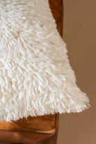 Close-up of a fluffy white rug on a wooden surface with a brown background