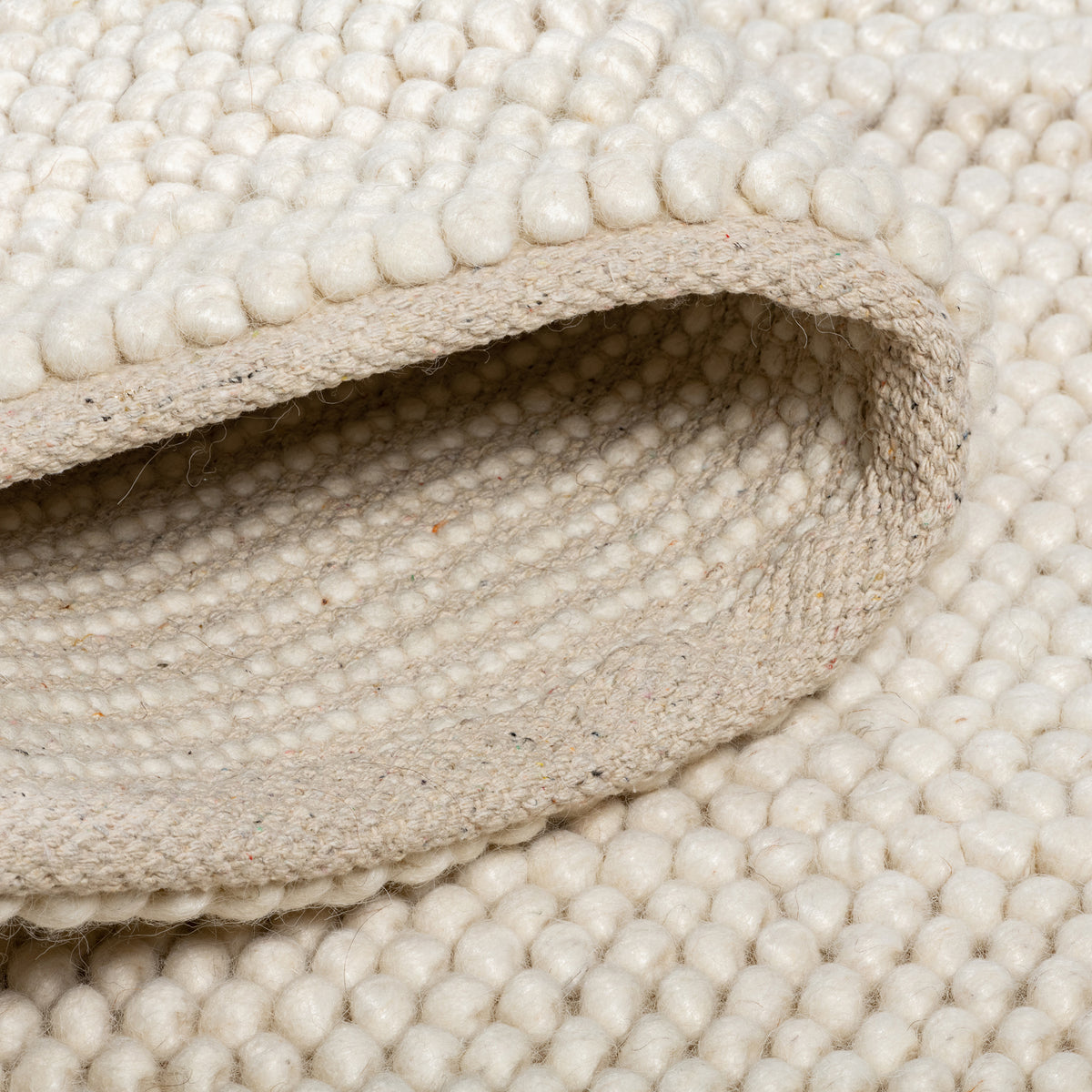 Close-up of the folded cream Felix handmade rug showing its thick, bobbly texture and canvas backing