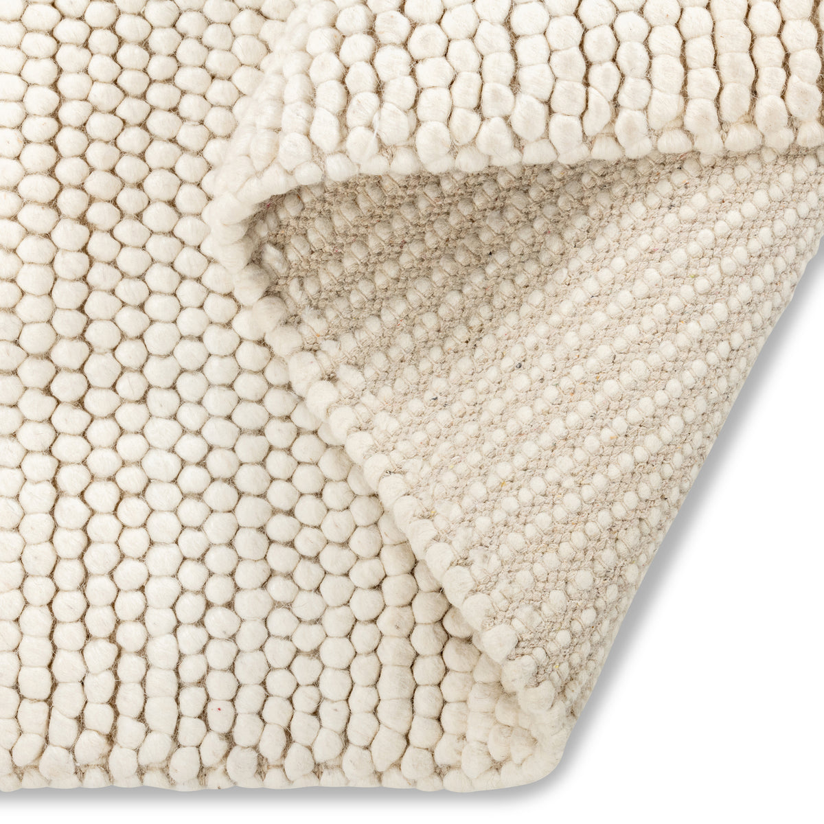 Folded corner of the cream Felix handmade textured rug, revealing its chunky pebble-like surface and sturdy backing