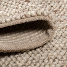 Close-up of the folded beige Felix handmade rug showing its thick, bobbly texture and sturdy canvas backing
