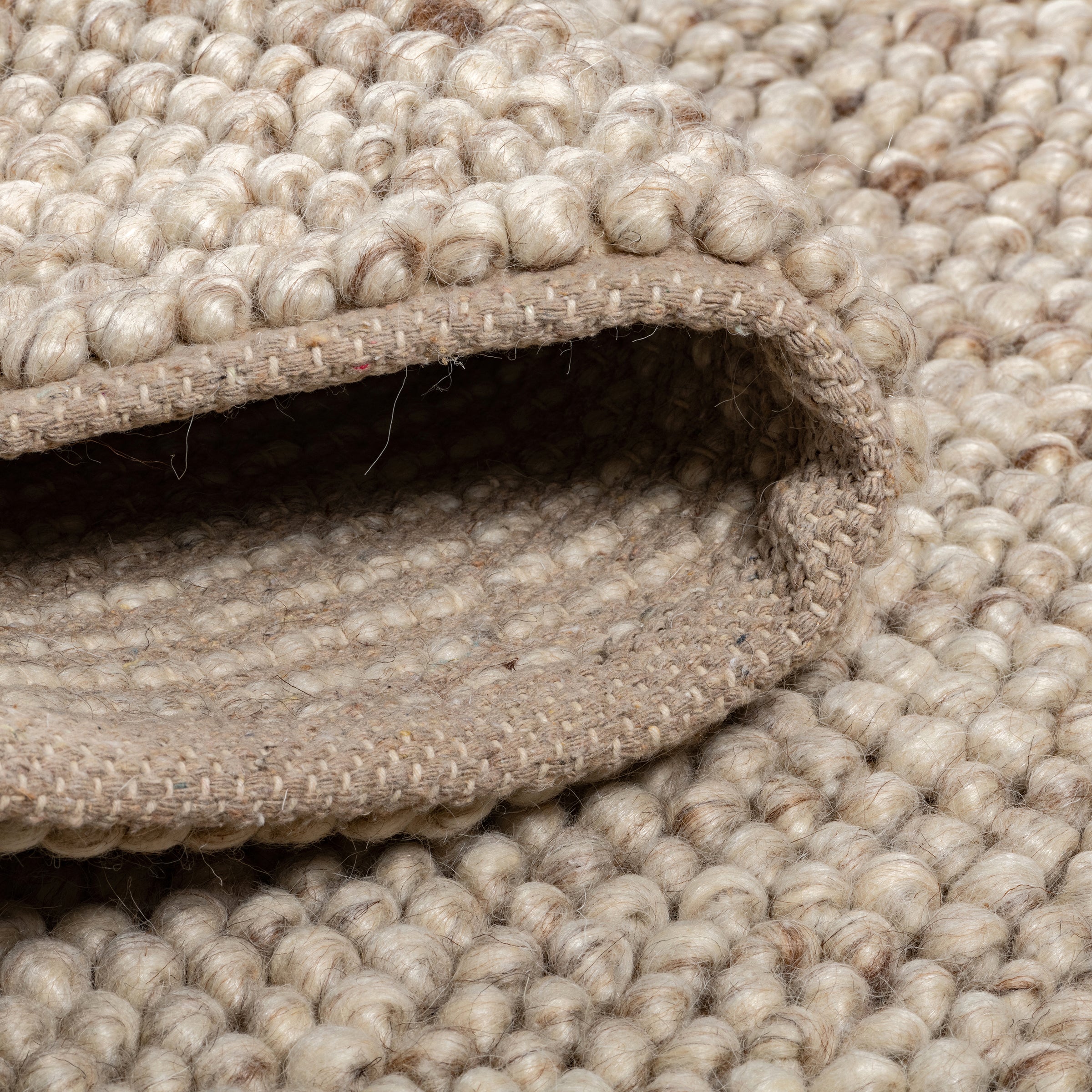 Close-up of the folded beige Felix handmade rug showing its thick, bobbly texture and sturdy canvas backing.